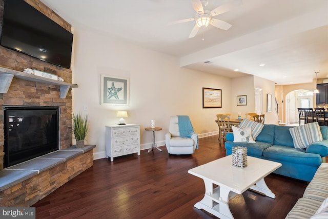 living room with a stone fireplace, ceiling fan, and dark hardwood / wood-style floors