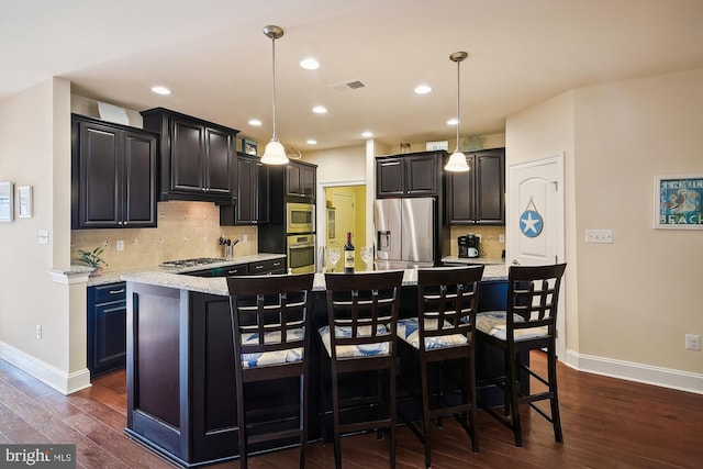 kitchen featuring stainless steel appliances, a kitchen island with sink, dark hardwood / wood-style floors, hanging light fixtures, and a breakfast bar area