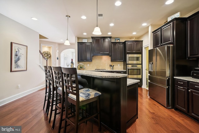 kitchen featuring light stone countertops, hanging light fixtures, dark hardwood / wood-style flooring, a kitchen bar, and appliances with stainless steel finishes