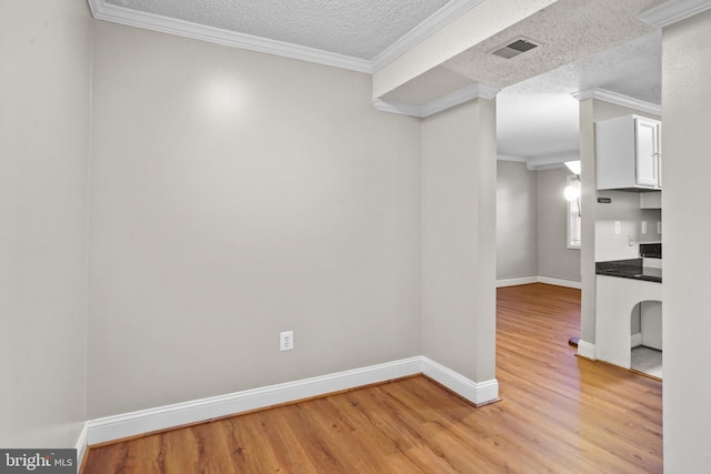 spare room featuring a textured ceiling, light hardwood / wood-style flooring, and ornamental molding