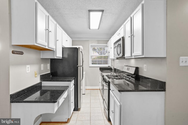 kitchen with appliances with stainless steel finishes, dark stone counters, a textured ceiling, light tile patterned floors, and white cabinets