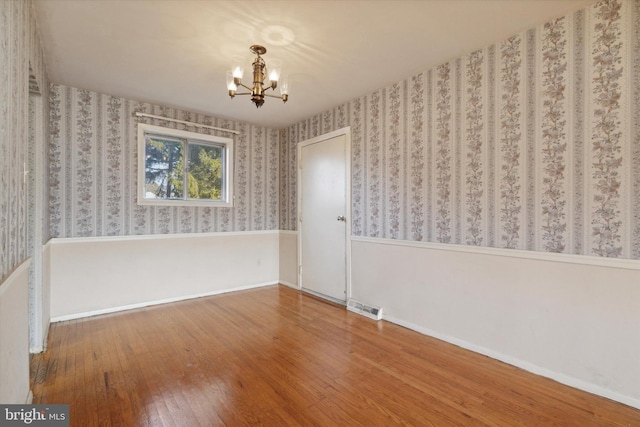 spare room with wood-type flooring and an inviting chandelier