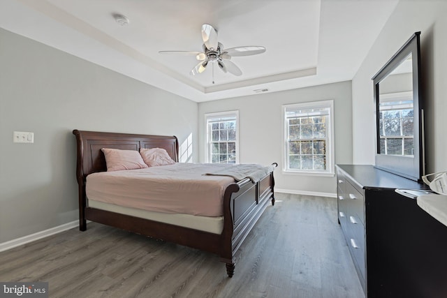 bedroom with ceiling fan, dark hardwood / wood-style flooring, and a raised ceiling