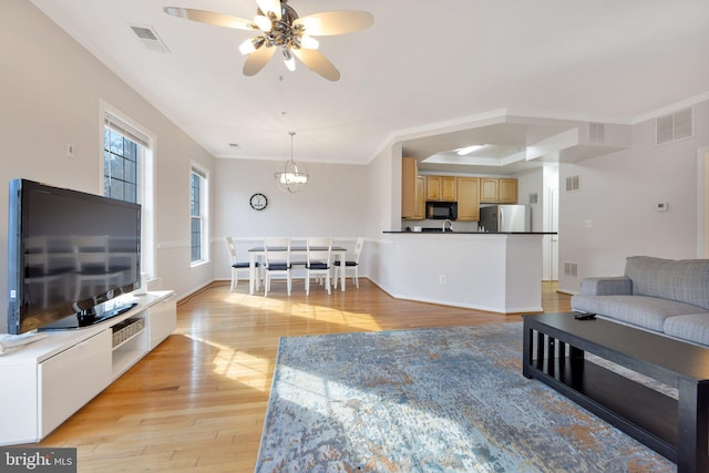 living room featuring ceiling fan with notable chandelier, ornamental molding, and light hardwood / wood-style flooring