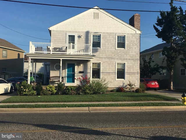 view of front of house featuring covered porch, a balcony, and a front lawn