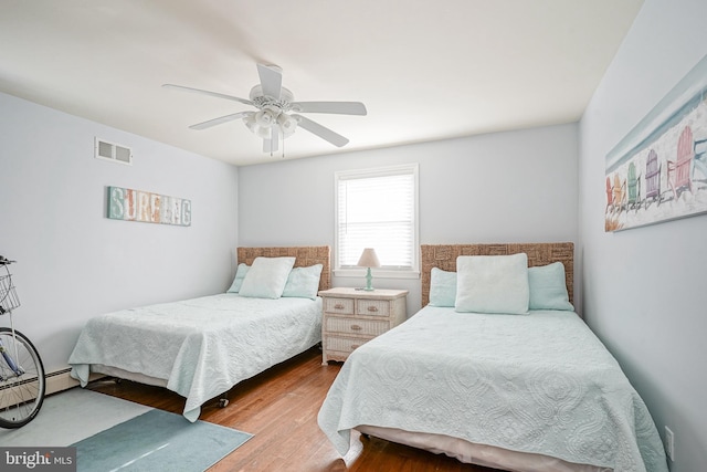 bedroom with wood-type flooring, ceiling fan, and a baseboard heating unit