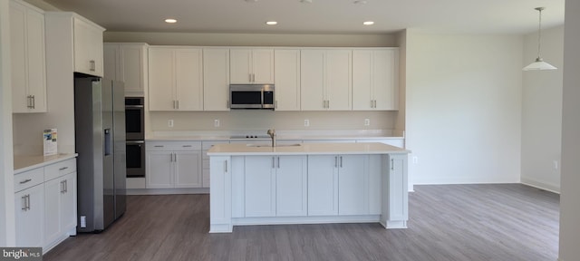 kitchen featuring white cabinets, light wood-type flooring, an island with sink, appliances with stainless steel finishes, and decorative light fixtures