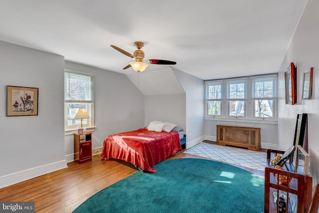 bedroom with radiator heating unit, light hardwood / wood-style floors, vaulted ceiling, and ceiling fan