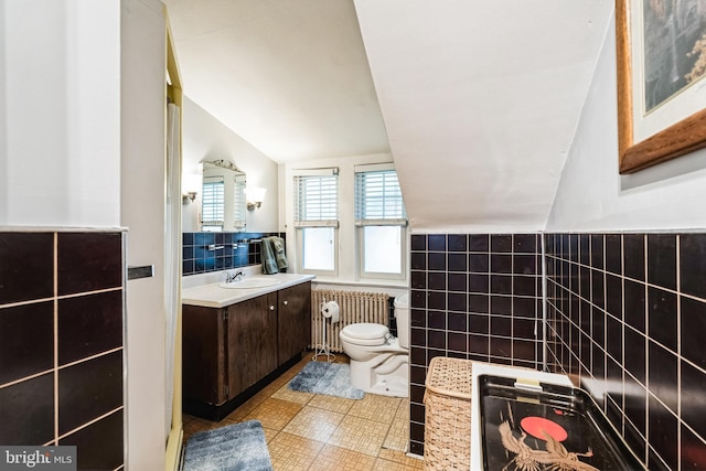 bathroom with radiator heating unit, tile patterned flooring, vaulted ceiling, vanity, and tile walls