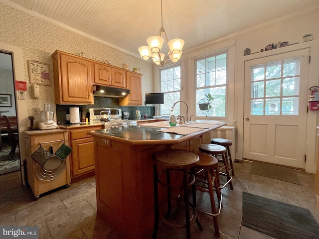 kitchen featuring ornamental molding, a chandelier, stainless steel stove, hanging light fixtures, and an island with sink