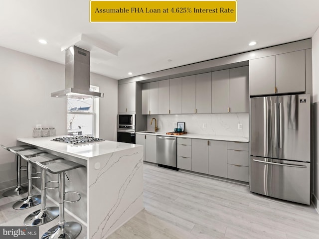 kitchen featuring gray cabinetry, a breakfast bar area, island range hood, kitchen peninsula, and stainless steel appliances