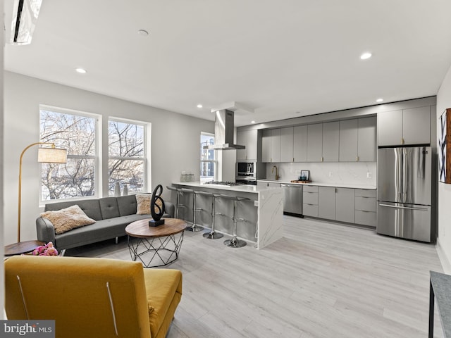 kitchen featuring gray cabinetry, a breakfast bar, wall chimney exhaust hood, and stainless steel appliances