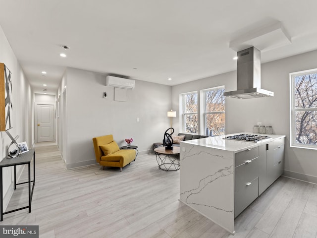 kitchen featuring a wall mounted air conditioner, stainless steel gas stovetop, wall chimney range hood, and light hardwood / wood-style flooring