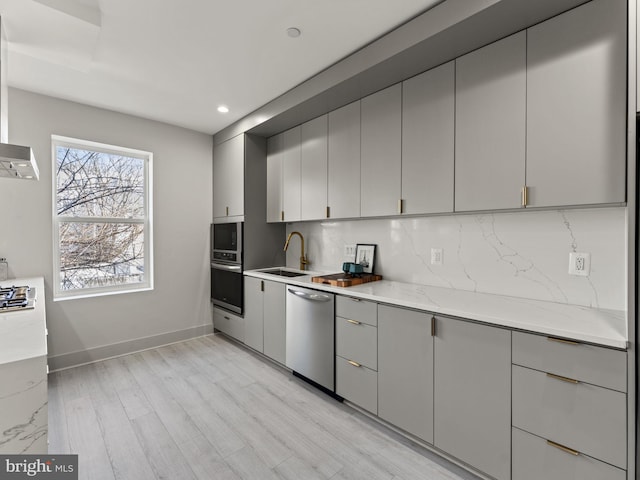 kitchen featuring gray cabinetry, sink, light stone counters, appliances with stainless steel finishes, and light wood-type flooring