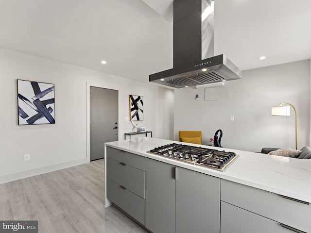 kitchen with wall chimney range hood, stainless steel gas cooktop, light stone counters, light hardwood / wood-style floors, and gray cabinets