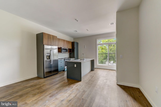 kitchen with appliances with stainless steel finishes, light hardwood / wood-style floors, a kitchen island with sink, and sink