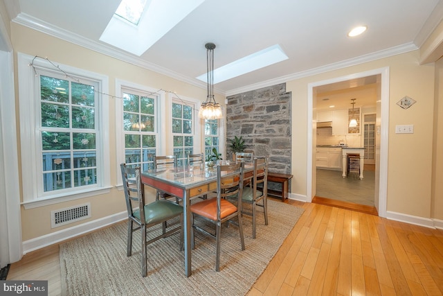 dining room featuring a skylight, crown molding, visible vents, light wood-style flooring, and baseboards