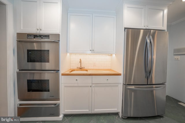 kitchen featuring stainless steel appliances, butcher block countertops, a sink, white cabinetry, and tasteful backsplash