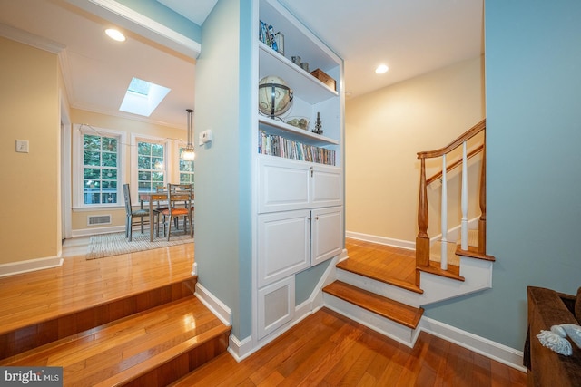 interior space with a skylight, visible vents, stairway, wood finished floors, and baseboards