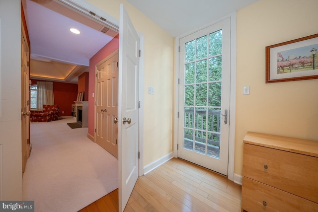 doorway featuring a fireplace with flush hearth, recessed lighting, light wood-style flooring, and baseboards