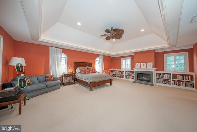 bedroom with carpet floors, a tray ceiling, multiple windows, and a glass covered fireplace