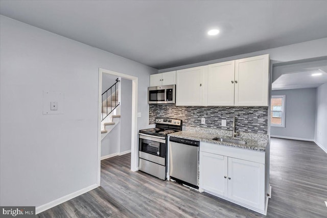 kitchen with light stone countertops, appliances with stainless steel finishes, sink, hardwood / wood-style flooring, and white cabinets