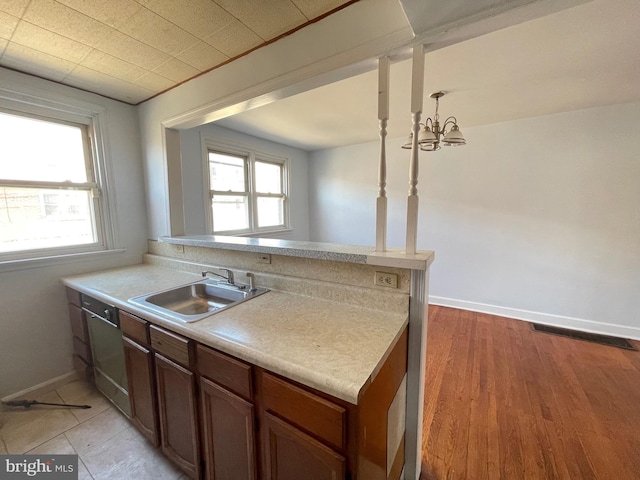 kitchen with kitchen peninsula, light hardwood / wood-style floors, a notable chandelier, and sink