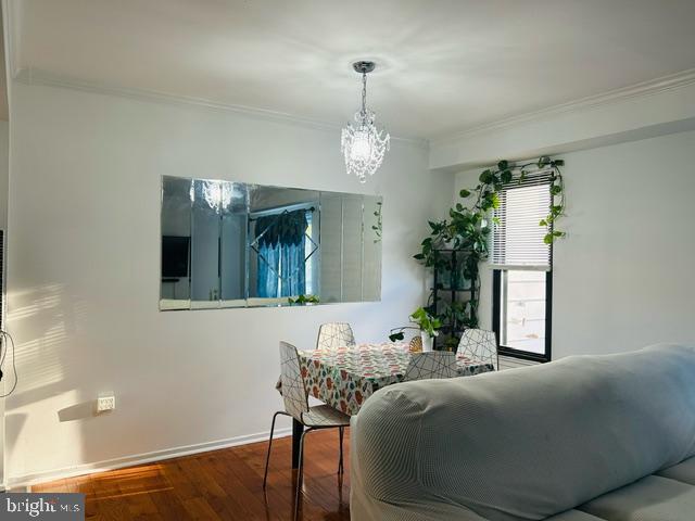 dining space with wood-type flooring, ornamental molding, and an inviting chandelier