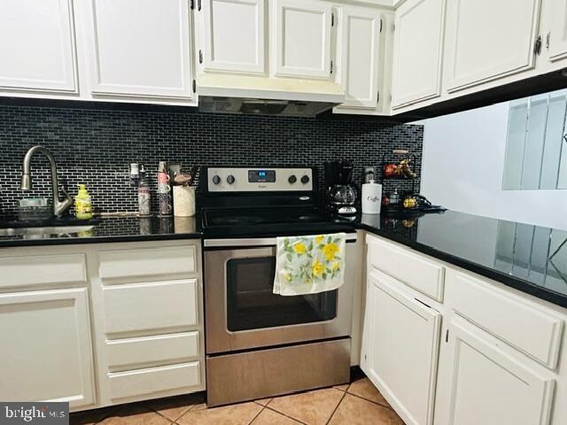 kitchen with stainless steel electric stove, sink, decorative backsplash, light tile patterned floors, and white cabinetry