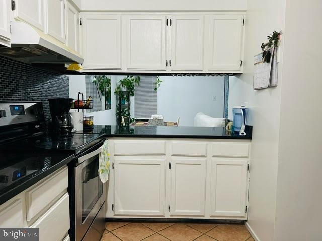 kitchen with decorative backsplash, light tile patterned floors, white cabinets, and stainless steel electric range