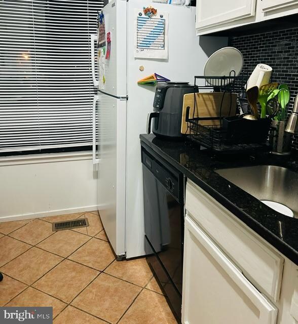 kitchen featuring backsplash, dark stone counters, light tile patterned floors, dishwasher, and white cabinetry