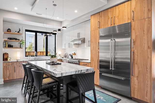 kitchen with built in fridge, a kitchen island, range, under cabinet range hood, and a kitchen breakfast bar