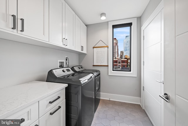 laundry room featuring washing machine and dryer, cabinet space, a city view, and baseboards