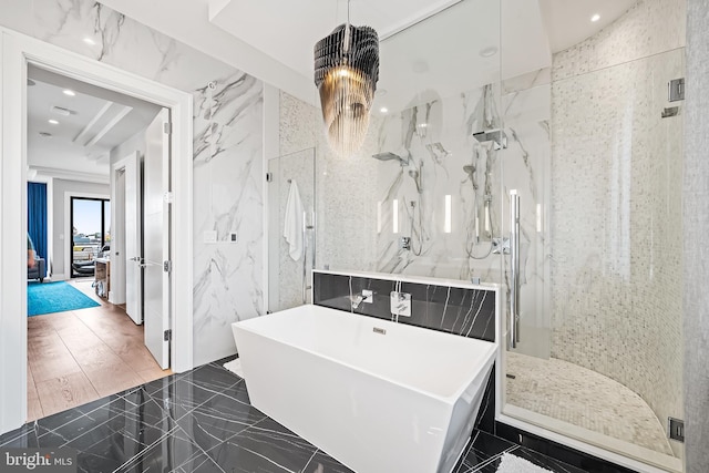 bathroom featuring marble finish floor, tile walls, a marble finish shower, a freestanding bath, and stone wall