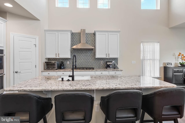 kitchen with a breakfast bar, white cabinetry, wall chimney range hood, and a healthy amount of sunlight