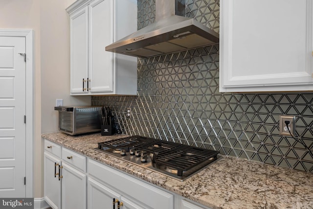 kitchen with light stone countertops, tasteful backsplash, wall chimney exhaust hood, stainless steel gas cooktop, and white cabinets