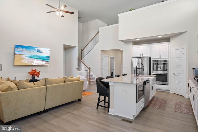 kitchen featuring high vaulted ceiling, white cabinets, a center island with sink, light hardwood / wood-style flooring, and appliances with stainless steel finishes