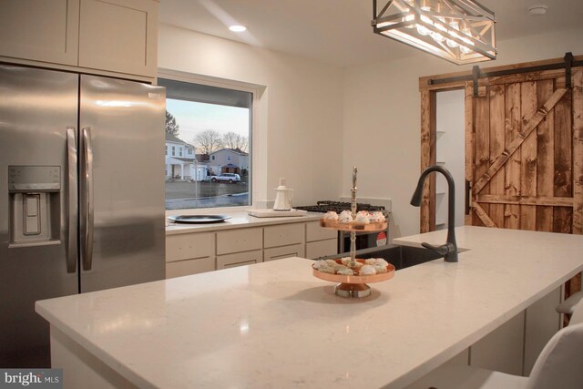 kitchen with sink, pendant lighting, a barn door, white cabinets, and stainless steel fridge with ice dispenser