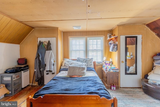 bedroom featuring wood walls, wood-type flooring, and vaulted ceiling