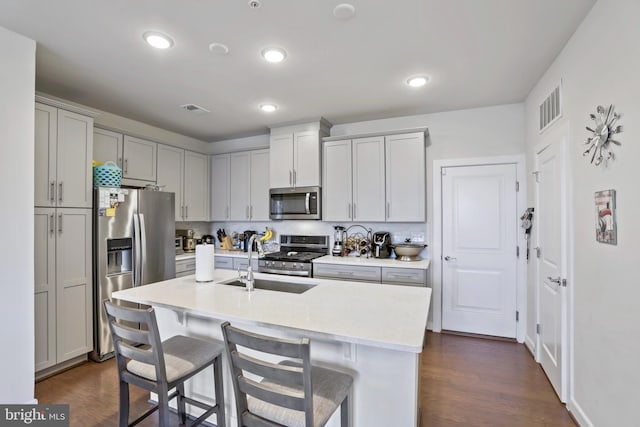 kitchen featuring sink, dark hardwood / wood-style floors, a kitchen bar, a center island with sink, and appliances with stainless steel finishes