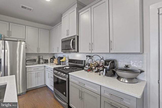 kitchen with light stone countertops, appliances with stainless steel finishes, decorative backsplash, gray cabinets, and dark hardwood / wood-style floors