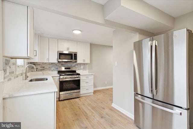 kitchen featuring tasteful backsplash, stainless steel appliances, sink, light hardwood / wood-style floors, and white cabinetry