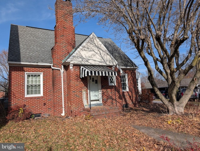 view of front facade featuring a shingled roof, brick siding, and a chimney