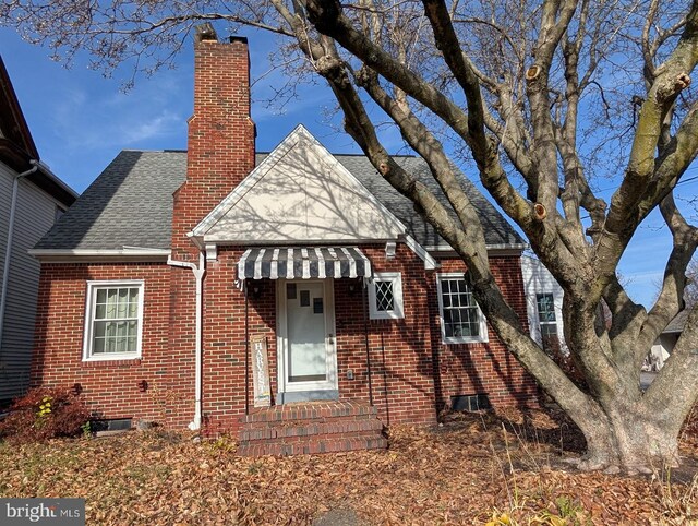 tudor-style house featuring brick siding, roof with shingles, and a chimney