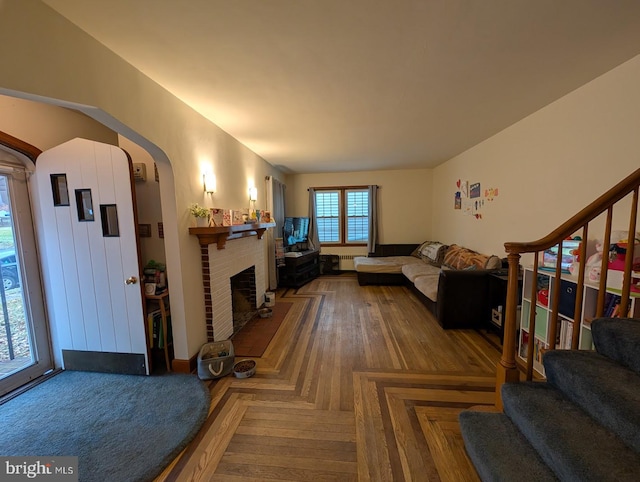 living area featuring a brick fireplace, stairway, and arched walkways