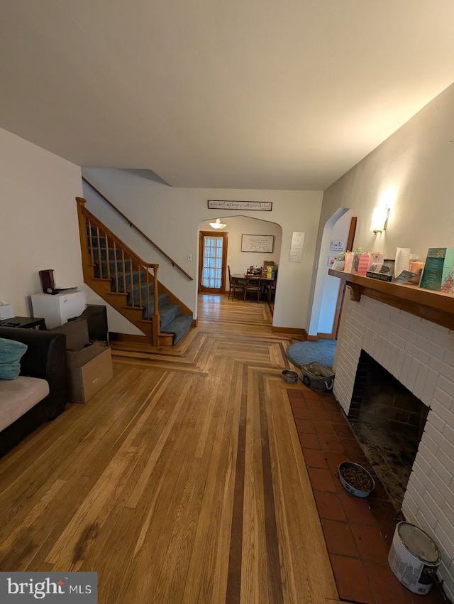 living area with stairway, wood finished floors, baseboards, a fireplace, and arched walkways