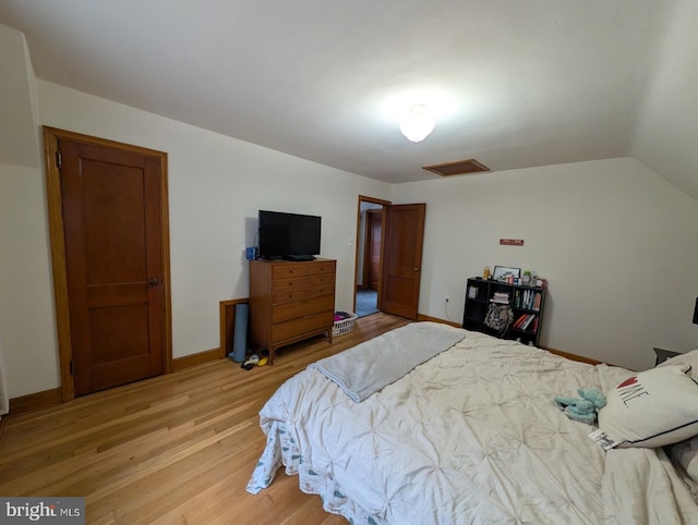 bedroom with baseboards, attic access, light wood-type flooring, and lofted ceiling