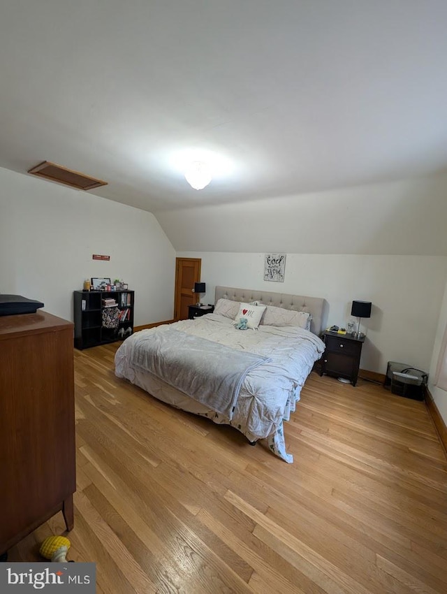 bedroom with visible vents, baseboards, attic access, lofted ceiling, and light wood-style flooring