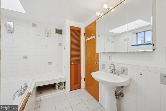 bathroom with tile walls, a relaxing tiled tub, tile patterned floors, and a skylight