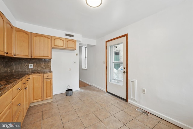 kitchen featuring light tile patterned floors, dark stone countertops, tasteful backsplash, and light brown cabinets